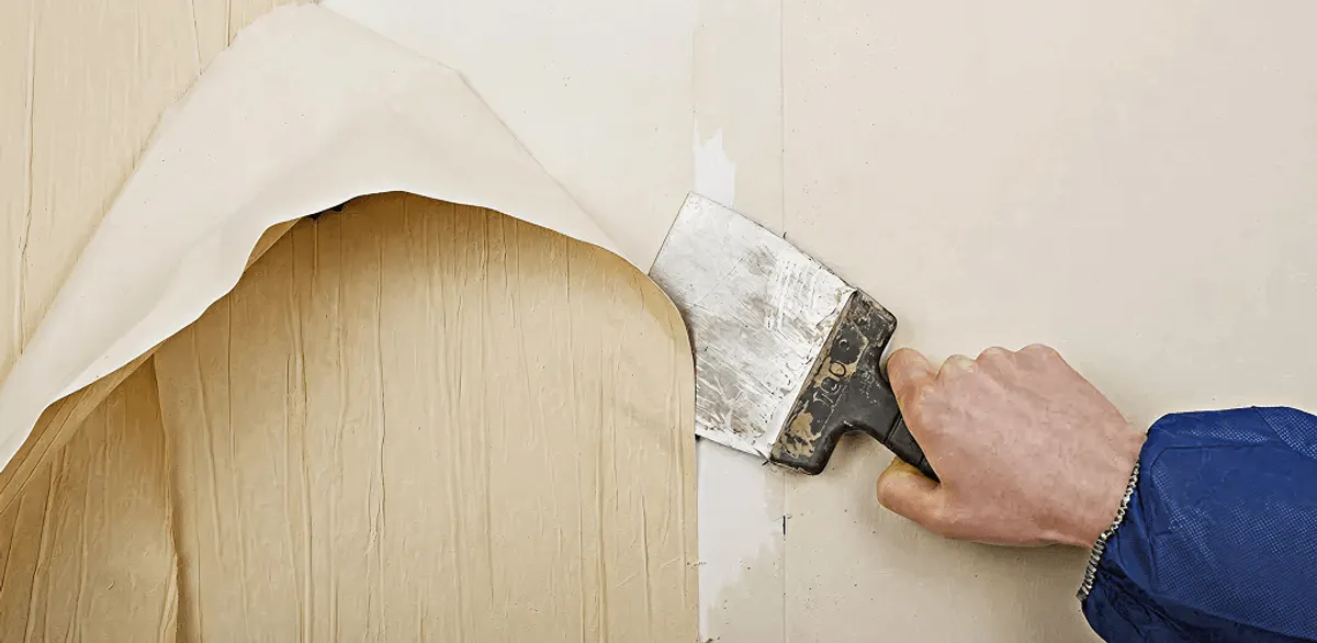 Handyman removing wallpaper with a scraper for wall preparation in Charlotte, NC